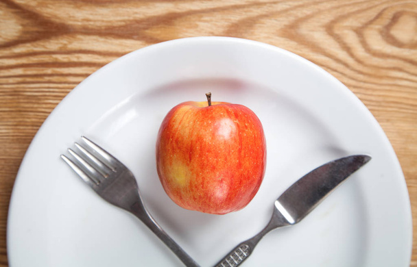 白い皿にフォークとナイフを入れた赤いリンゴ。ダイエットコンセプト - 写真・画像
