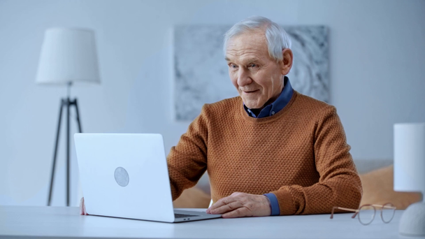 Selektiver Fokus eines glücklichen Rentners mit Videoanruf und winkender Hand beim Blick auf den Laptop zu Hause  - Filmmaterial, Video