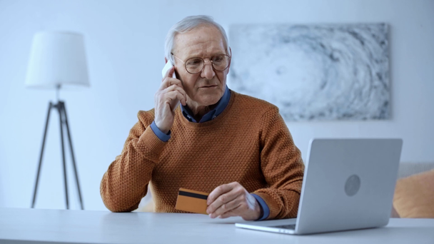 вибірковий фокус старшого чоловіка в окулярах розмовляє смартфоном і розмовляє, тримаючи кредитну картку біля ноутбука
  - Кадри, відео