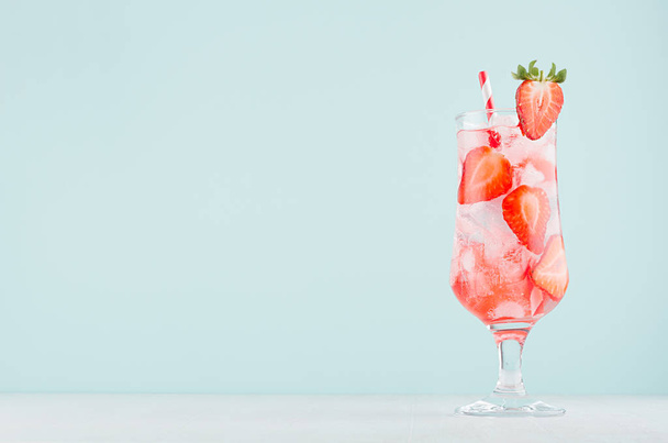 Healthy fresh tonic with strawberry slices, ice cubes, soda, striped straw in misted glass on white wood table, pastel green color background. - Foto, Imagen