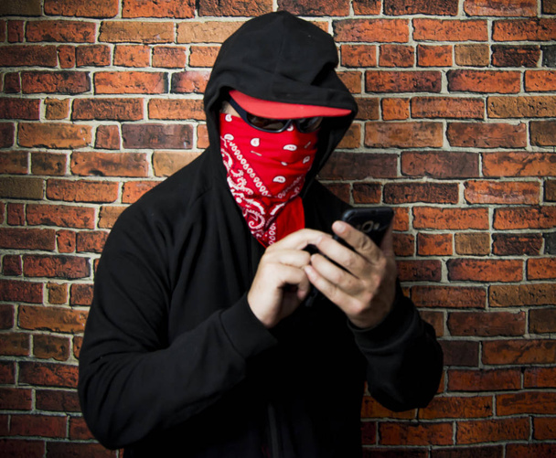 Ukryty człowiek z kapturem i szalik za pomocą telefonu komórkowego przed  - Zdjęcie, obraz
