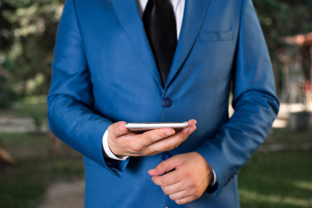 Geschäftskonzept mit Mann in der Hand Handy mit Touchscreen. Geschäftsmann hält Laptop in der Hand. Geschäftsmann in blauer Anzug steht mit Handy in der Hand. - Foto, Bild