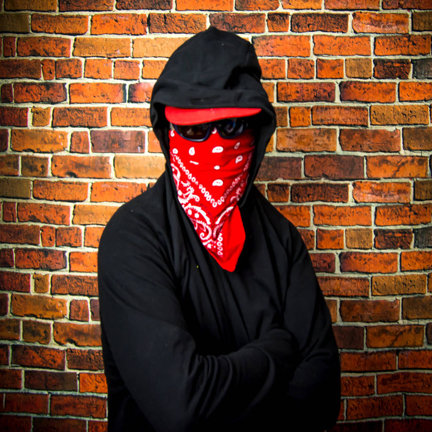 Hombre oculto con capucha y bufanda delante de una pared de ladrillo
 - Foto, Imagen