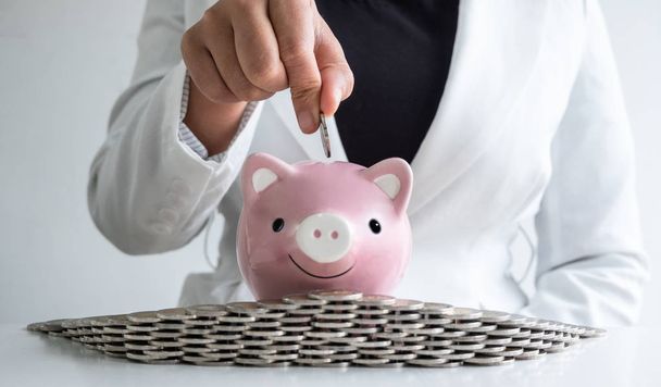 vrouw hand putting Coin in roze Piggy Bank met munten bunker, Step up Protect bedrijf naar succes en besparing voor pensioen concept - Foto, afbeelding