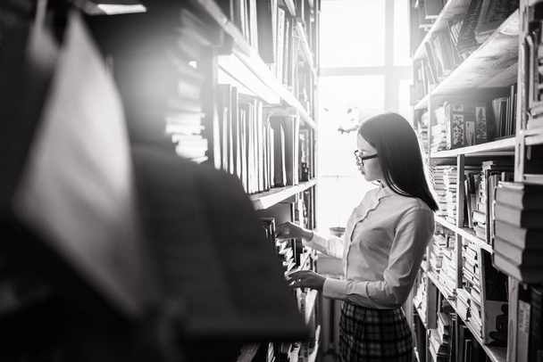 Adolescente eligiendo libros en la biblioteca - blanco y negro, vista monocromática
. - Foto, Imagen