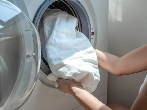 Woman's hand putting dirty white linen shirt in washing machine. - Photo, Image