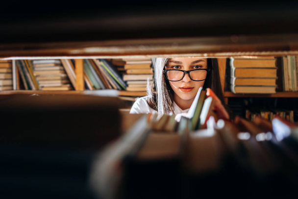 Teenager-Mädchen sucht Bücher in Bibliothek aus - Blick durch Regale. - Foto, Bild