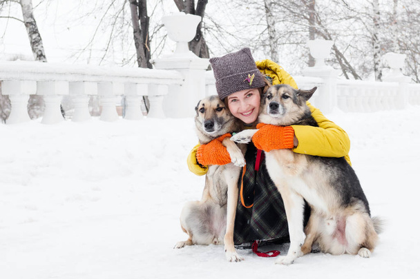 Portrait of beautiful smiling young woman with her two dogs in a snowy winter park. - Foto, Imagen