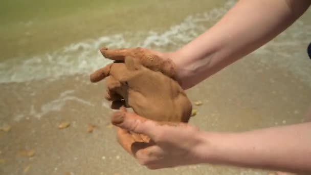 Κοντινό πλάνο των χεριών που κάνουν πηλό σε μια παραλία θάλασσα, άμμο και κύματα ως φόντο, το καλοκαίρι και το ταξίδι έννοια. - Πλάνα, βίντεο