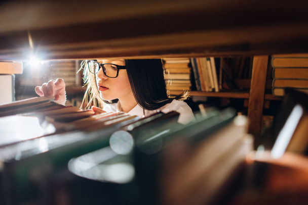 Adolescente eligiendo libros en la biblioteca - ver a través de estantes
. - Foto, Imagen