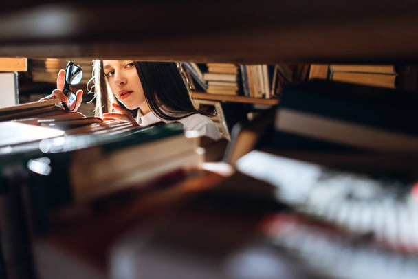 Teenager-Mädchen sucht Bücher in Bibliothek aus - Blick durch Regale. - Foto, Bild