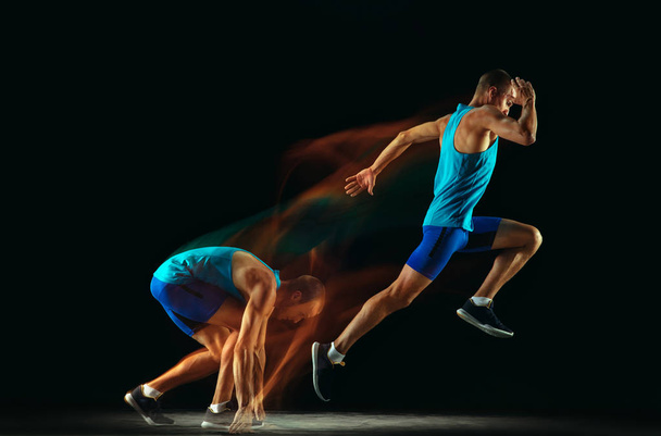Professional male runner training isolated on black studio background in mixed light - Photo, image