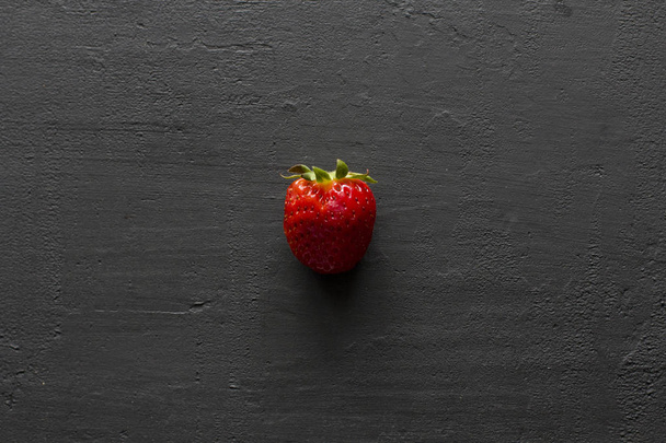 Jeden czerwony piękny truskawka zbliżenie, na czarnym ciemnym betonie  - Zdjęcie, obraz