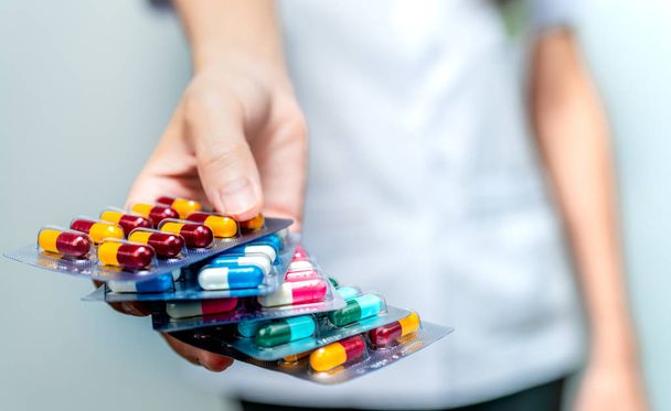 Gyógyszerész vagy orvos kezében csomag antibiotikum kapszulát tabletták és amely beteg vagy emberek. Antibiotikum kábítószer túlhasználat. Antimikrobiális szerekkel szembeni rezisztencia. Közösségi gyógyszerész. Illatszertár háttere. - Fotó, kép