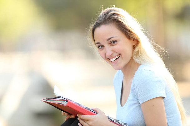 Happy student holding folder looking at camera in a park - Фото, зображення