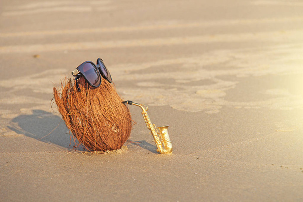 Кокос на пляже в солнцезащитных очках играет на золотом альте
 - Фото, изображение