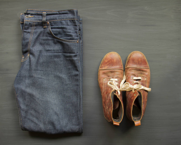 Jeans with brown leather boots over wooden floor black backgroun - Foto, imagen