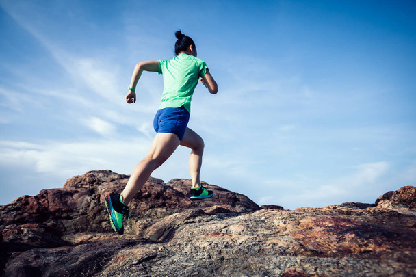 Young fitness woman trail runner running to rocky mountain top on seaside - Foto, Imagem