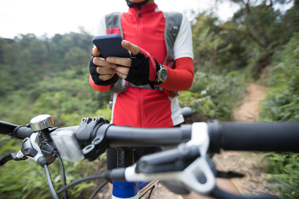 Équitation sur une colline d'été, tenant le téléphone mobile, en utilisant l'application en ligne pour rechercher les coordonnées GPS tout en faisant du vélo dans la forêt par une journée ensoleillée
 - Photo, image