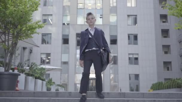 Cute little boy wearing a business suit with case walking in the city. Child as adult. - Imágenes, Vídeo