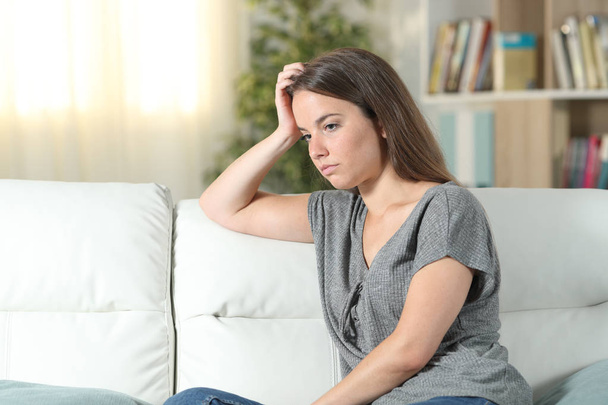 Worried woman looking away on a couch at home - Foto, imagen
