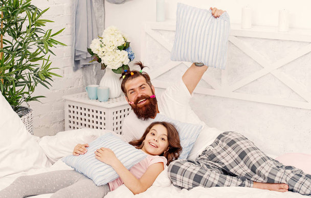 Man bearded hipster with childish hairstyle colorful ponytails and daughter in pajamas. Guy and girl relaxing in bedroom. Pajamas style. Having fun pajamas party. Slumber party. Happy fatherhood - Photo, Image