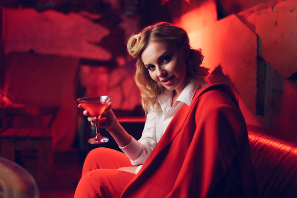 Kuva nuori blondi punaisessa takissa cocktail kädessään yökerhossa
 - Valokuva, kuva