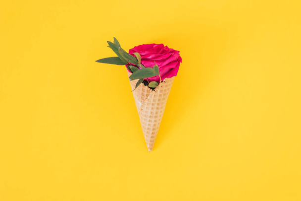 Flat lay Ice Cream Cone with pink rose on yellow background, copy space - Photo, Image