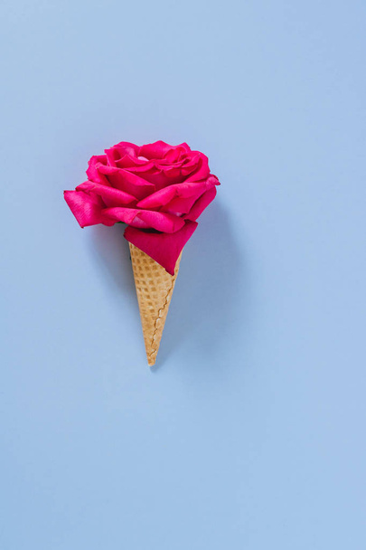 Flat lay Ice Cream Cone with pink rose on blue background, copy space - Fotó, kép