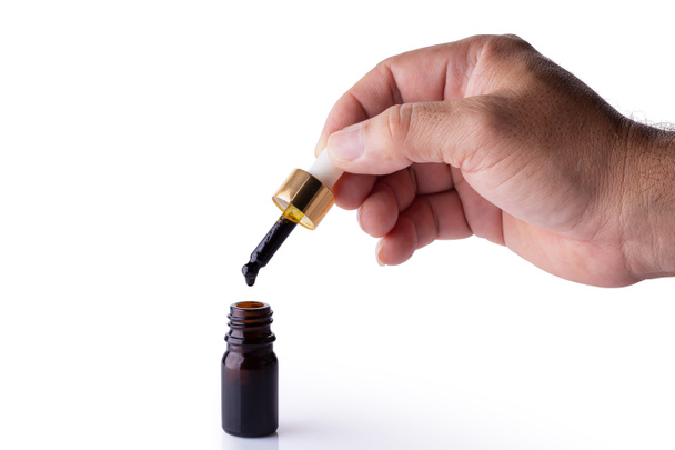 Hand holding pipette of Cannabis oil over a bottle. - Photo, Image