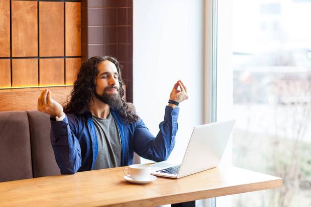 successful handsome young adult man freelancer in casual style sitting in cafe with laptop and holding hands like meditation while doing yoga in office cafe  - Foto, Bild