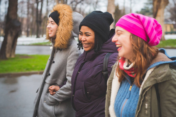 drie jonge vrouwen lachen en wandelen buiten in stedelijk park - Foto, afbeelding