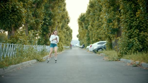 A teenage girl in rollerblades skating on the road - looking at the phone - Footage, Video