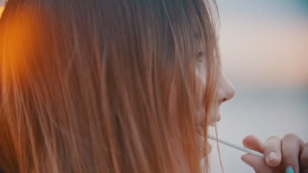 A portrait of teenage girl looking around and eating a lollipop on sunset - Imágenes, Vídeo