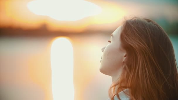 Ένα έφηβο κορίτσι με ανοιχτό καφέ κοιτάζοντας γύρω και κοιτάζοντας στην κάμερα στο ηλιοβασίλεμα - Πλάνα, βίντεο