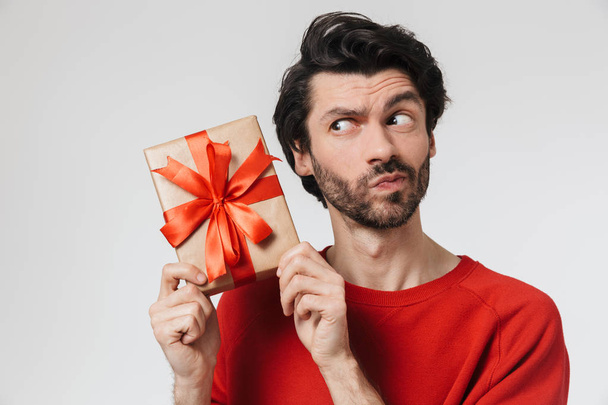 Handsome young excited man posing isolated over white wall background holding present gift box. - Foto, afbeelding