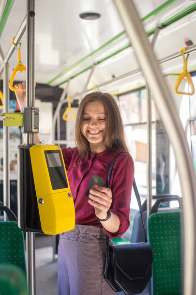 Female Woman paying conctactless with smartphone for the public transport in the tram. Yellow ticket machine in the modern tram - Фото, зображення