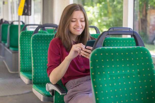 Young woman passenger standing with  smartphone while moving in the modern tram, enjoying trip at the public transport - Foto, Imagen