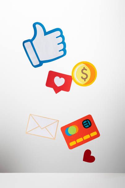 kleurrijke papier knippen met envelop, munt, creditcard, harten en duim omhoog op witte achtergrond - Foto, afbeelding