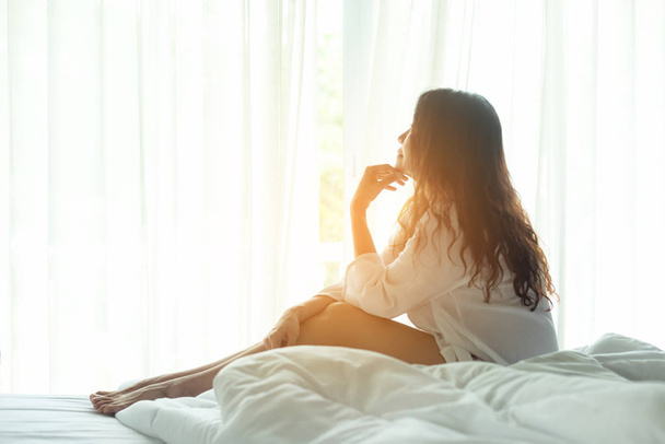 Asian woman in bedroom relax after wake up near window, sunny morning. Lifestyle Concept. - Photo, Image