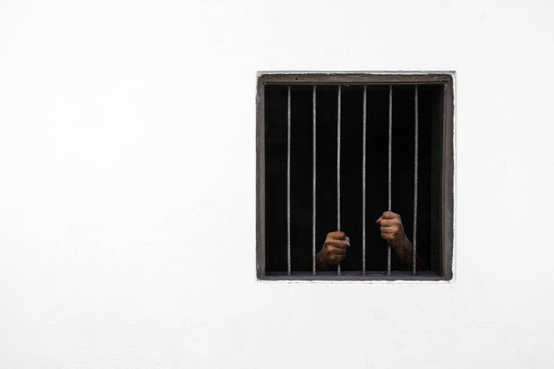 Las manos del prisionero en la barra oxidada de la ventana y la celda de la prisión
 - Foto, imagen