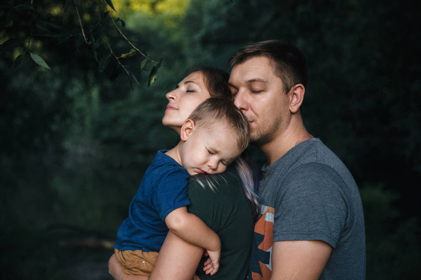 Happy joyful young family father, mother and little son outdoors, hugging together in summer park - Foto, afbeelding