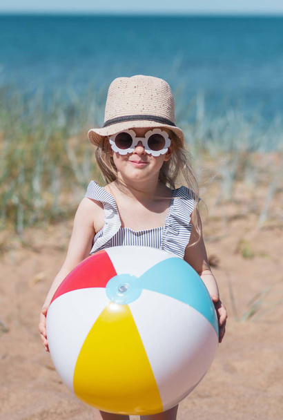 Kislány kalapban játszani a strandon a labdát, napsütéses nyári napon. Nyaralási koncepció - Fotó, kép