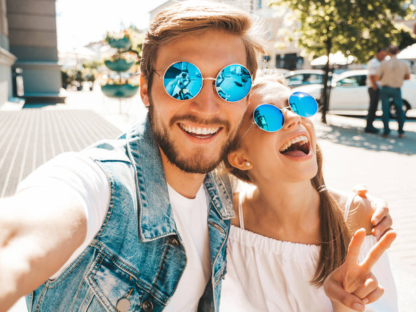 Smiling beautiful girl and her handsome boyfriend in casual summer clothes.Happy family taking selfie self portrait of themselves on smartphone camera in sunglasses.Having fun on the street background - Φωτογραφία, εικόνα