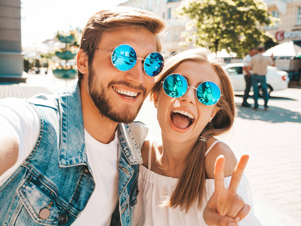 Smiling beautiful girl and her handsome boyfriend in casual summer clothes.Happy family taking selfie self portrait of themselves on smartphone camera in sunglasses.Having fun on the street background - Zdjęcie, obraz