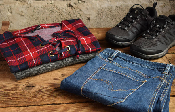 Мужская повседневная одежда. Мужская обувь, одежда и аксессуары на деревянном фоне - свитер, джинсы, кроссовки. Вид сверху. Плоский лежал
 - Фото, изображение