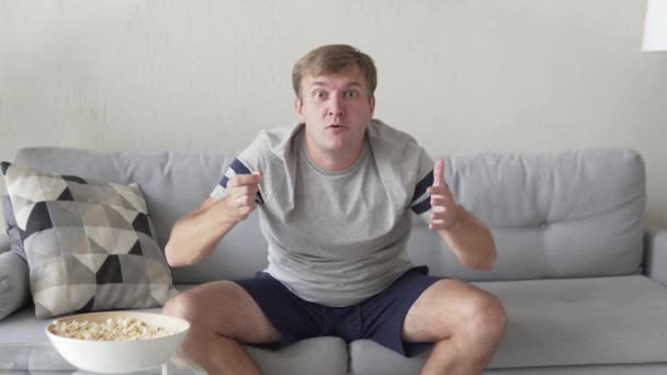 zábavný fanoušek s popcornem doma na gauči - Záběry, video