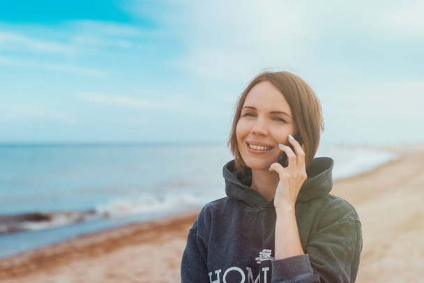 La femme sourit et communique par téléphone sur le bord de la mer, l'océan
. - Photo, image