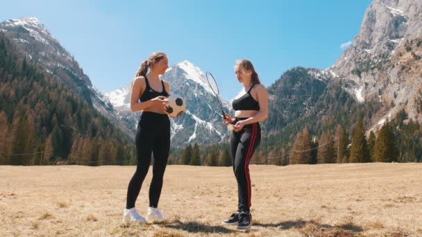 A pályán két fiatal, sportos, egy ütő és egy futballlabda tartó nő áll-Dolomitok, Olaszország - Felvétel, videó