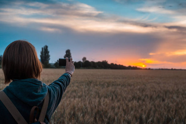 A woman takes a photo of a sunset on a wheat field. - Valokuva, kuva